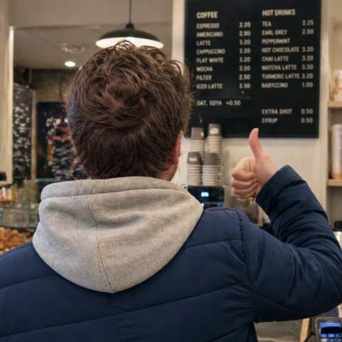 Man giving a thumbs up at a coffee shop counter