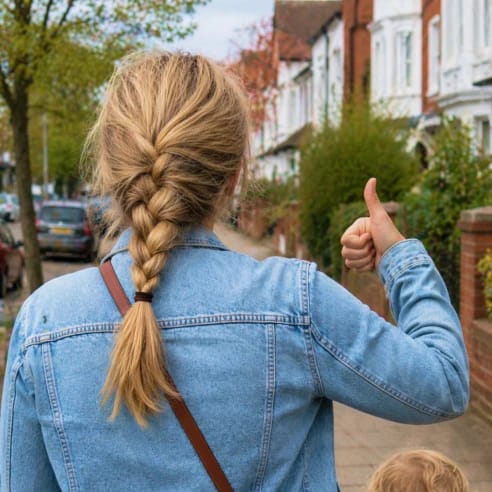 Woman with a braid giving a thumbs up on a residential street